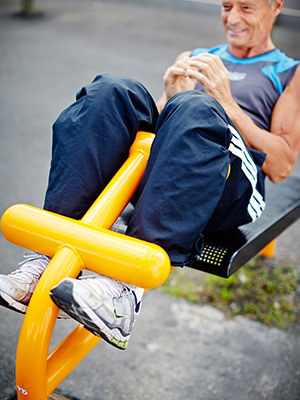 Man completes sit ups on a workout bench at an outdoor gym area.